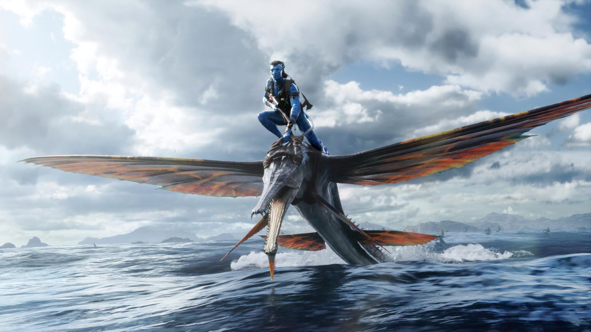 Ein Filmfoto aus James Camerons Fantasyfilm "Avatar: The Way of Water". Ein Angehöriger des Na'vi-Volkes reitet auf einem flugsauierähnlichen großen Tier über das Wasser. Die Na'vi haben blaue Haut und lange Haare. Ein Filmfoto aus James Camerons Fantasyfilm "Avatar: The Way of Water". Ein Angehöriger des Na'vi-Volkes reitet auf einem flugsauierähnlichen großen Tier über das Wasser. Die Na'vi haben blaue Haut und lange Haare.