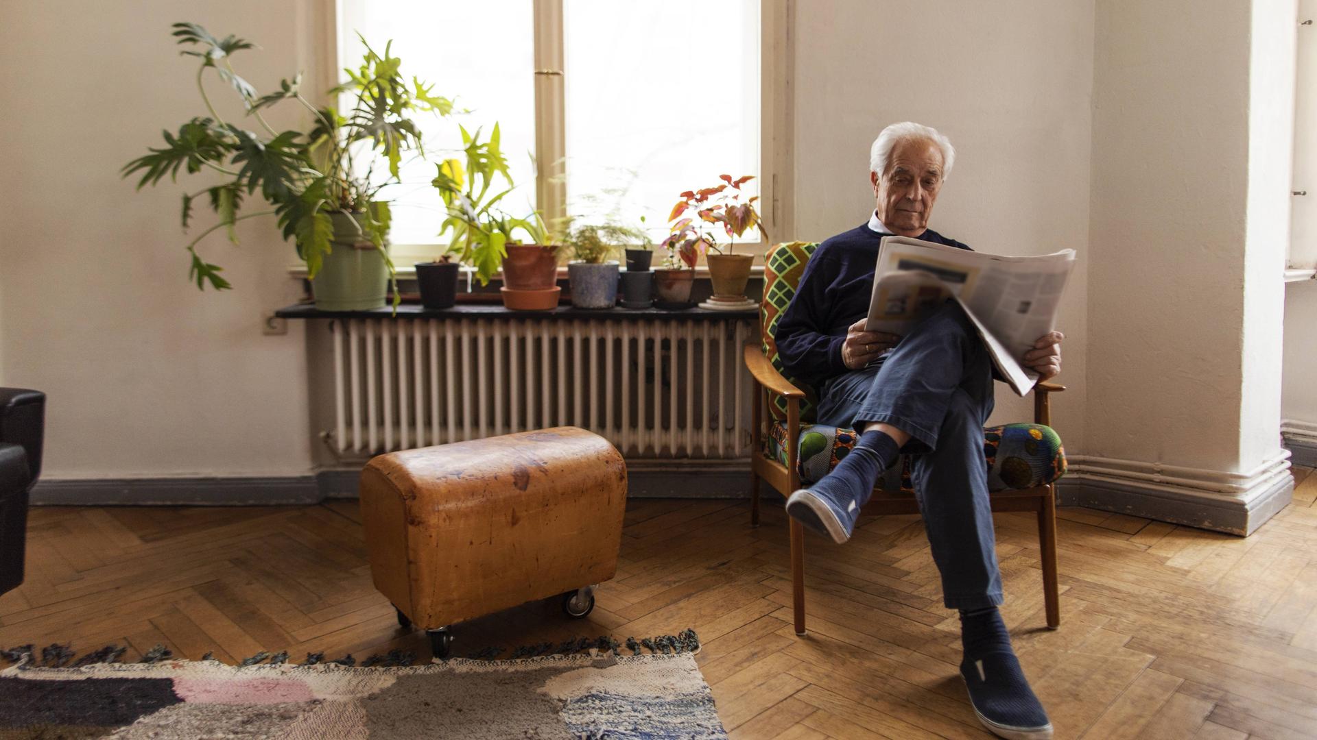 Ein älterer Mann sitzt auf einem Stuhl in einer Altbauwohnung und liest Zeitung. Ein älterer Mann sitzt auf einem Stuhl in einer Altbauwohnung und liest Zeitung.