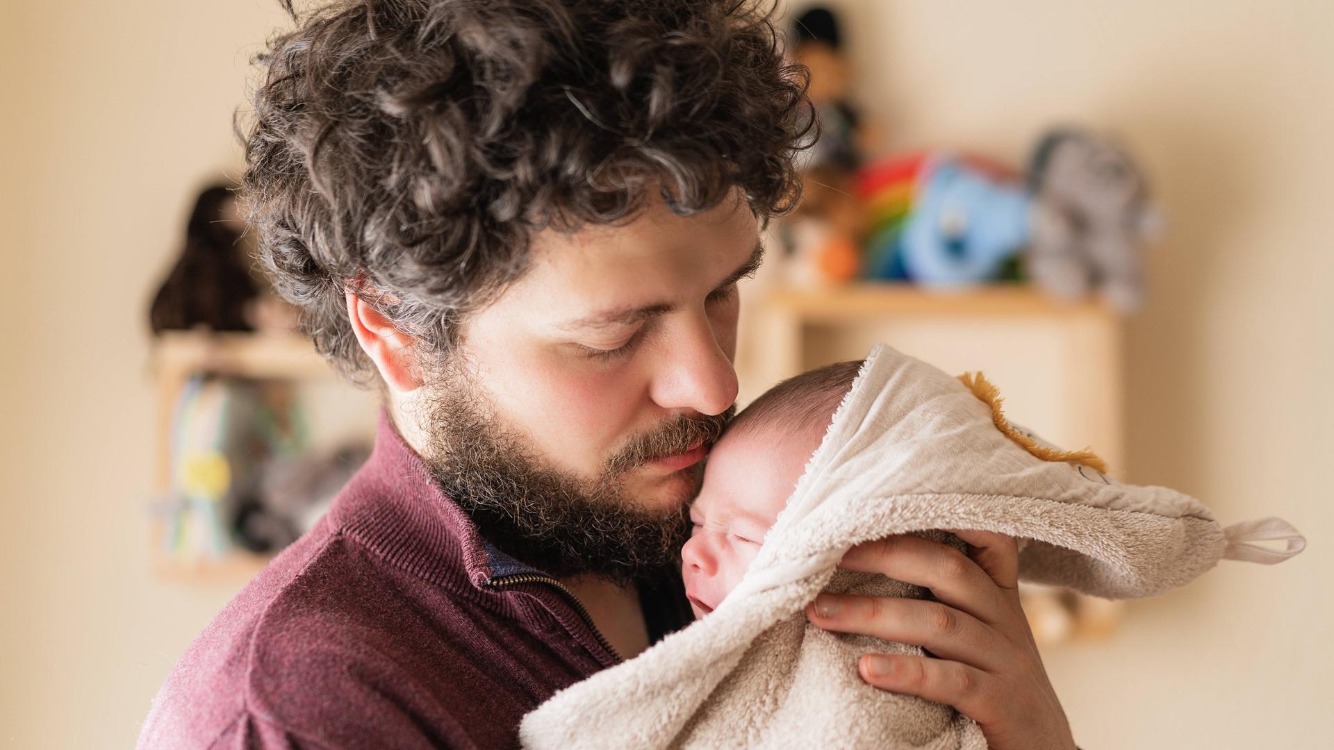 Ein bärtiger Vater hält liebevoll ein Baby im Arm. Ein bärtiger Vater hält liebevoll ein Baby im Arm.