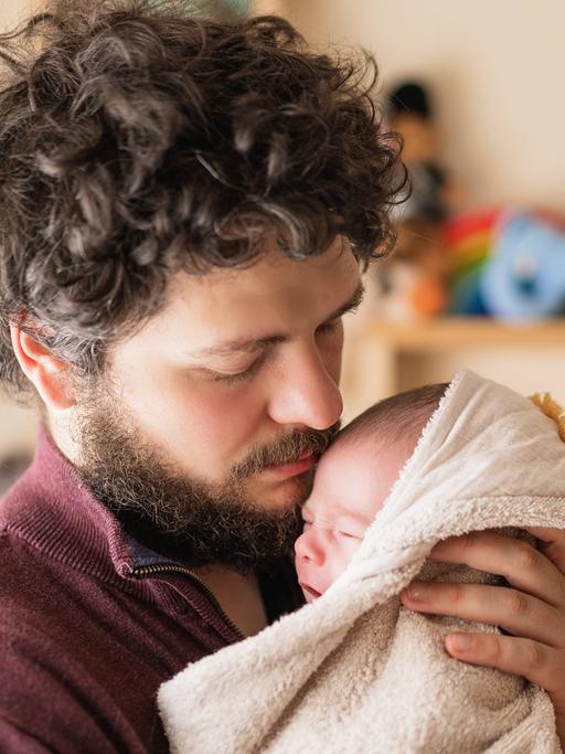 Ein bärtiger Vater hält liebevoll ein Baby im Arm.