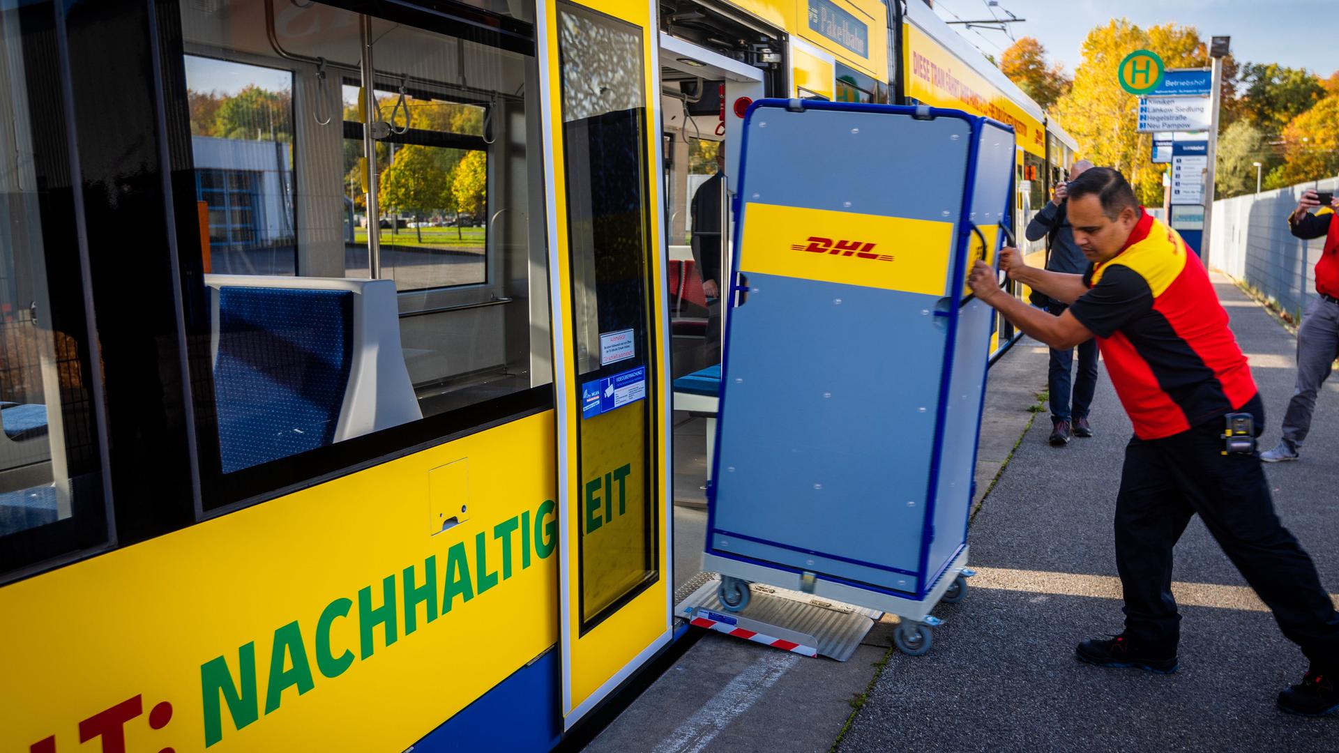 Ein Mitarbeiter der Deutschen Post schiebt einen Transportwagen für Pakete in eine Straßenbahn.