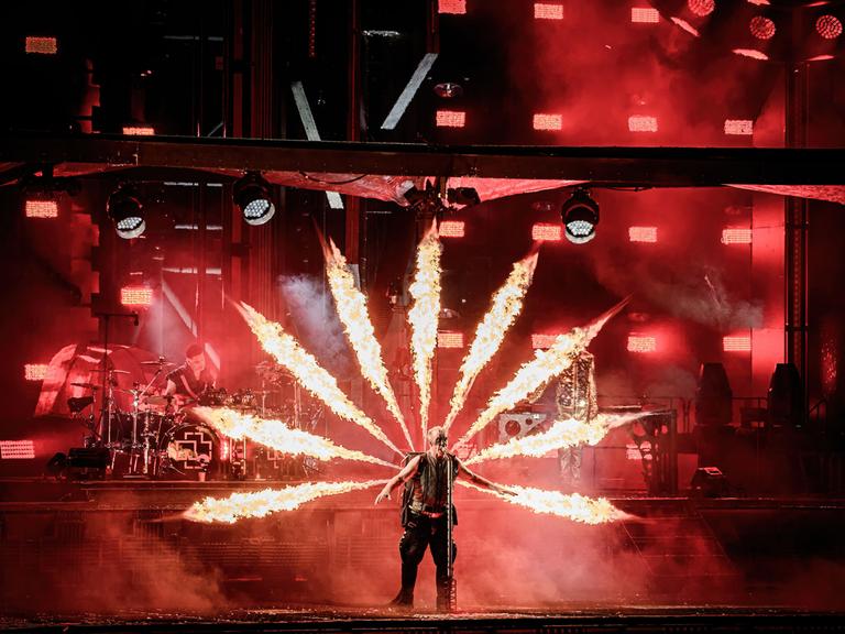 Rammstein-Sänger Till Lindemann ist von Feuerfontänen umgeben, die sternförmig aus einem Kasten auf seinem Rücken schießen.