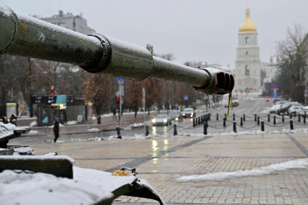 Ein Panzer steht links im Bild; im Hintergrund eine Kirche mit einer goldenen Kuppel und Autos, die auf der Straße fahren. Es ist winterlich, ein paar Schneehaufen liegen links und rechts der Straße. Ein Panzer steht links im Bild; im Hintergrund eine Kirche mit einer goldenen Kuppel und Autos, die auf der Straße fahren. Es ist winterlich, ein paar Schneehaufen liegen links und rechts der Straße.
