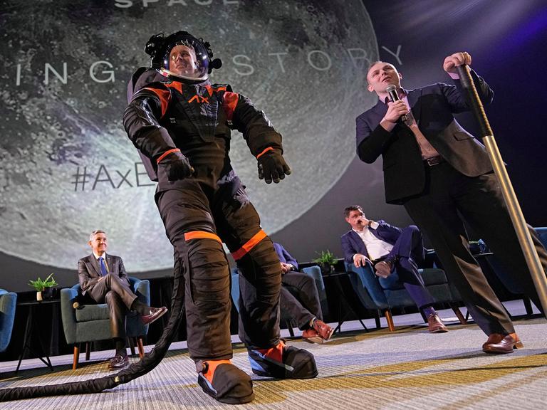 Jim Stein trägt einen schwarzen Raumanzug und steht stolz auf einer Bühne.