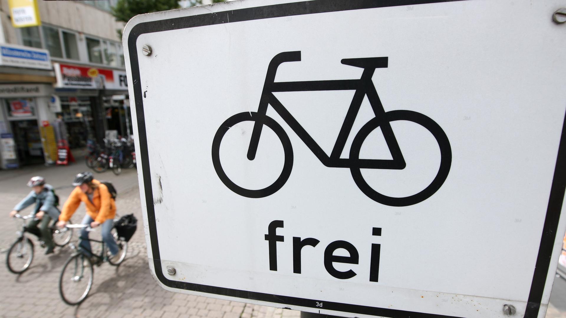 Fahrradfahrer radeln auf einer Straße in Münster unter einem Verkehrsschild mit dem Zeichen "Fahrrad frei". Fahrradfahrer radeln auf einer Straße in Münster unter einem Verkehrsschild mit dem Zeichen "Fahrrad frei".