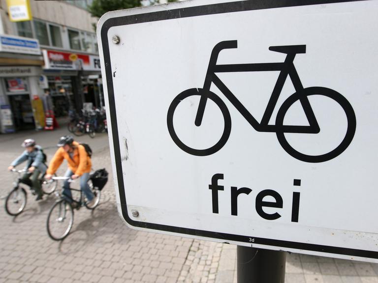 Fahrradfahrer radeln auf einer Straße in Münster unter einem Verkehrsschild mit dem Zeichen "Fahrrad frei".