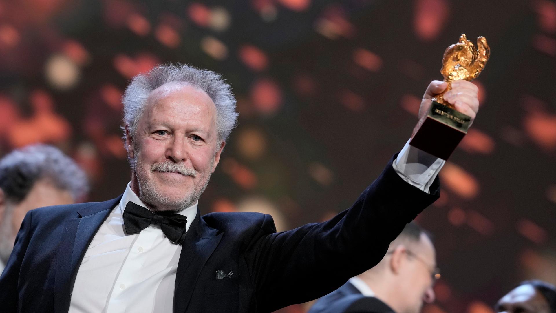 Nicolas Philibert steht auf der Bühne von der Berlinale und hält seinen Preis hoch. Nicolas Philibert steht auf der Bühne von der Berlinale und hält seinen Preis hoch.