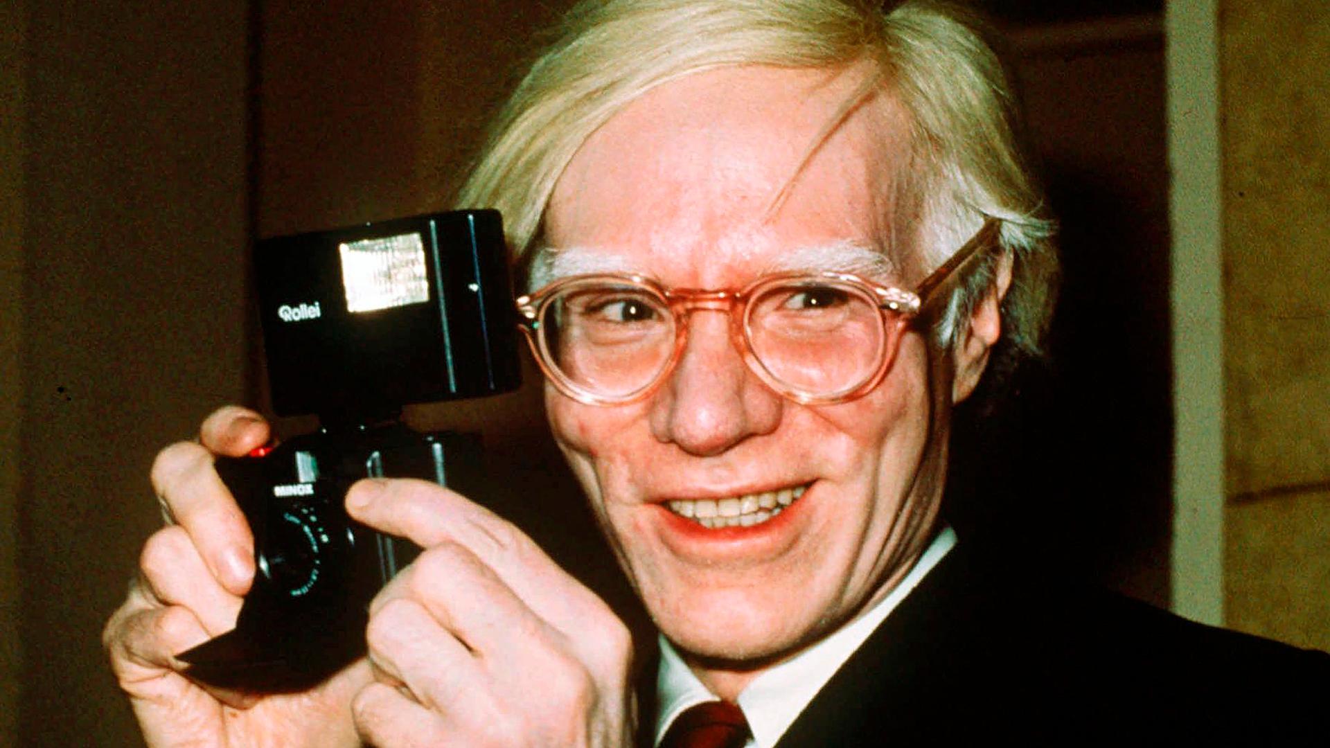 Der Künstler Andy Warhol mit einer Kamera in den Händen. Der Künstler Andy Warhol mit einer Kamera in den Händen.
