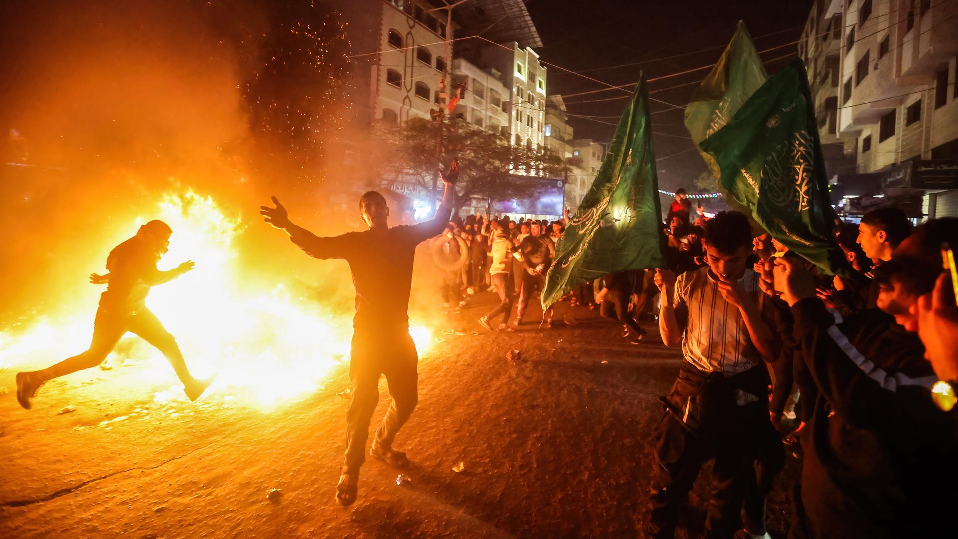 Menschen stehen auf einer Straße in Gaza und umkreisen jubelnd ein Feuer, in dem sie Flaggen und andere Zeichen Israels verbrennen. Menschen stehen auf einer Straße in Gaza und umkreisen jubelnd ein Feuer, in dem sie Flaggen und andere Zeichen Israels verbrennen.