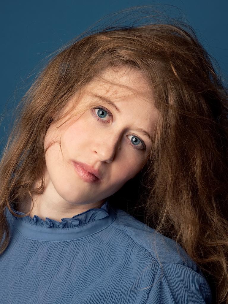 Wir sehen eine Frau, die einen blauen Pullover trägt und in die Kamera guckt. 
