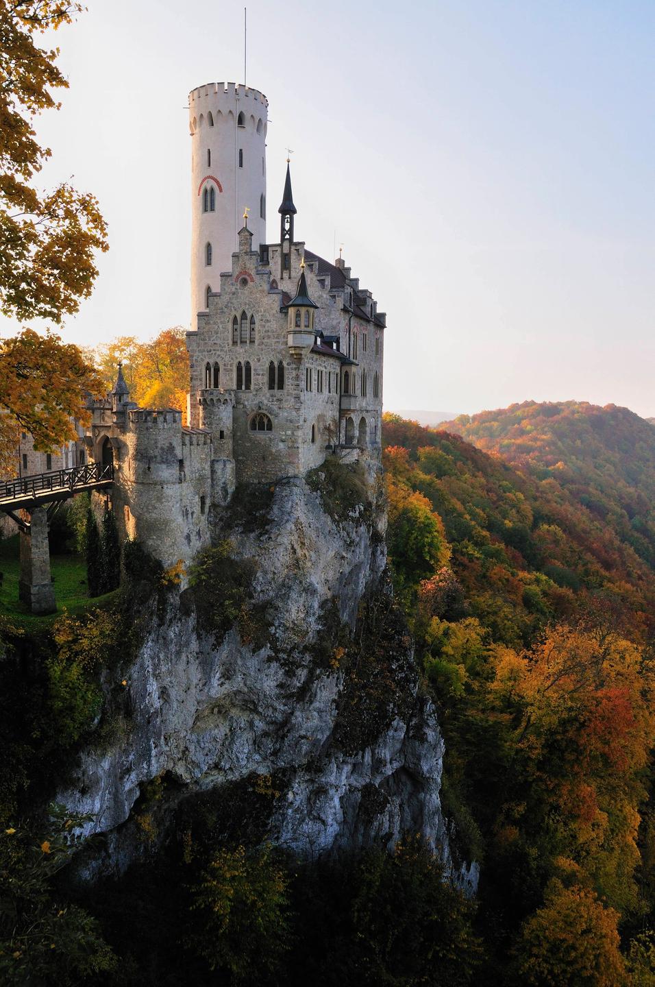 Das Romantik-Schloss Lichtenstein auf der Schwäbischen Alb. Ein Schloss mit Turm und Zinnen auf einem Felsen. Im Hintergrund sind die dicht bewachsenen Hügel der Schwäbischen Alb zu sehen.