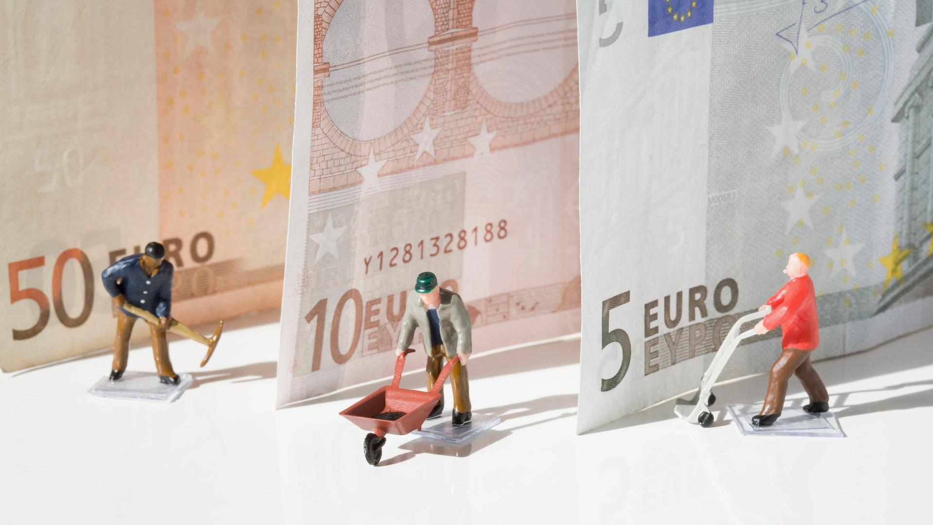 Kleine Arbeiterfiguren stehen vor drei Euro-Banknoten. Kleine Arbeiterfiguren stehen vor drei Euro-Banknoten.