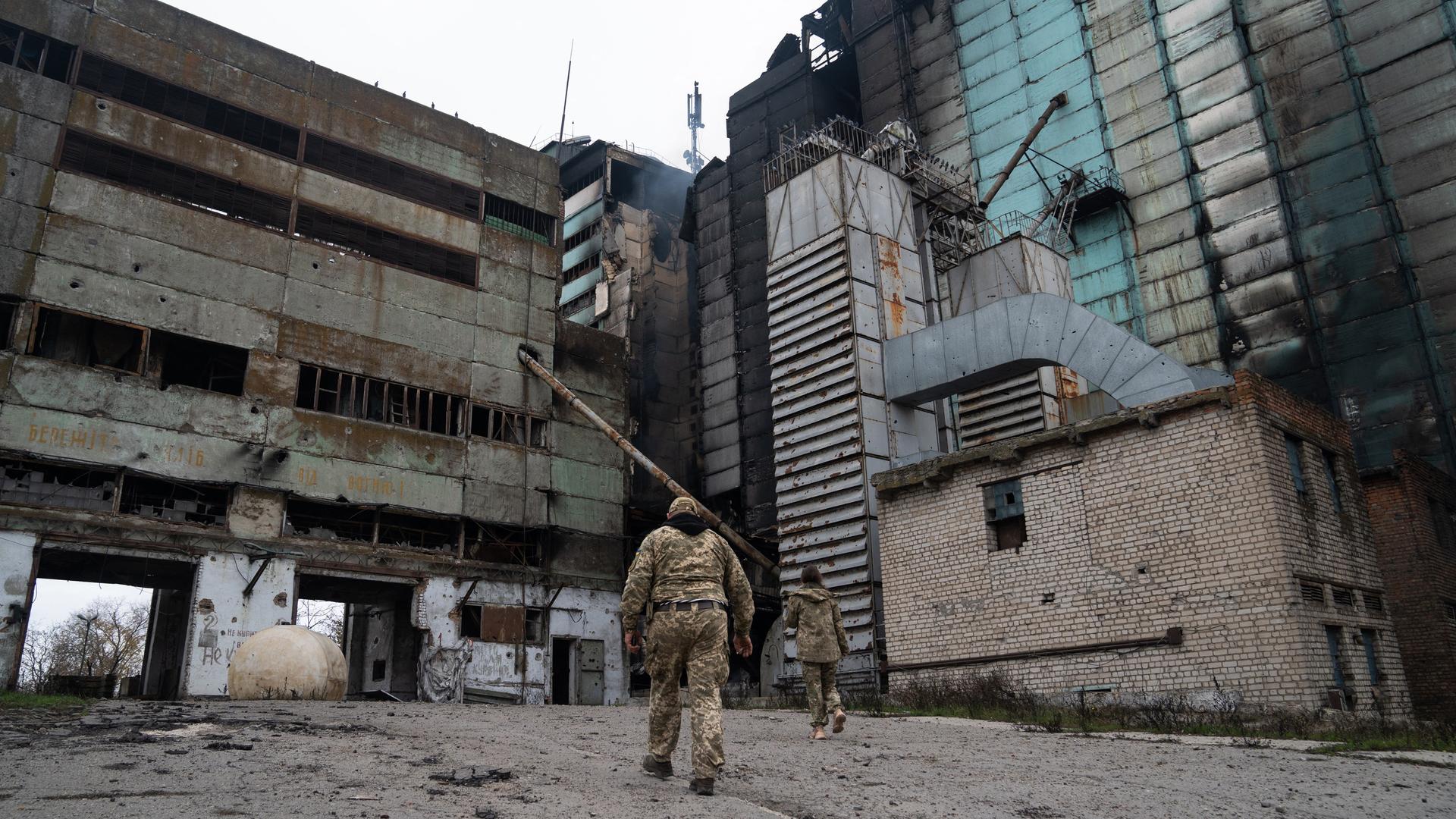 Ukrainische Soldaten laufen auf ein ausgebranntes Industriegebäude im Gebiet Cherson zu. In der Mitte raucht es noch.