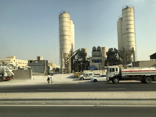 Vor einem Zementwerk in Doha laufen zwei Menschen an der Straße entlang.