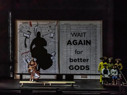 Bühnenbild mit riesigem aufgeklapptem Buch vor dem eine Tänzerin und eine Musikgruppe stehen