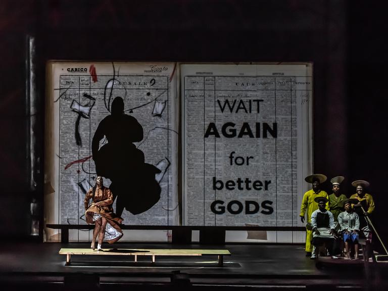 Bühnenbild mit riesigem aufgeklapptem Buch vor dem eine Tänzerin und eine Musikgruppe stehen