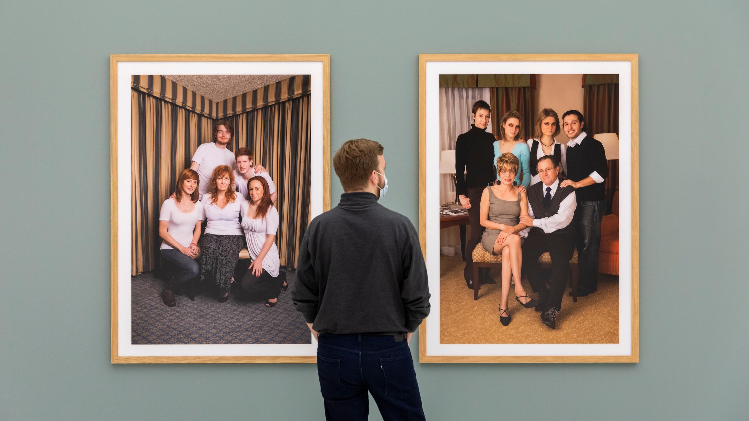 Ein Mann steht in einer Ausstellung vor zwei Fotografien, die jeweils eine Familie porträtieren.