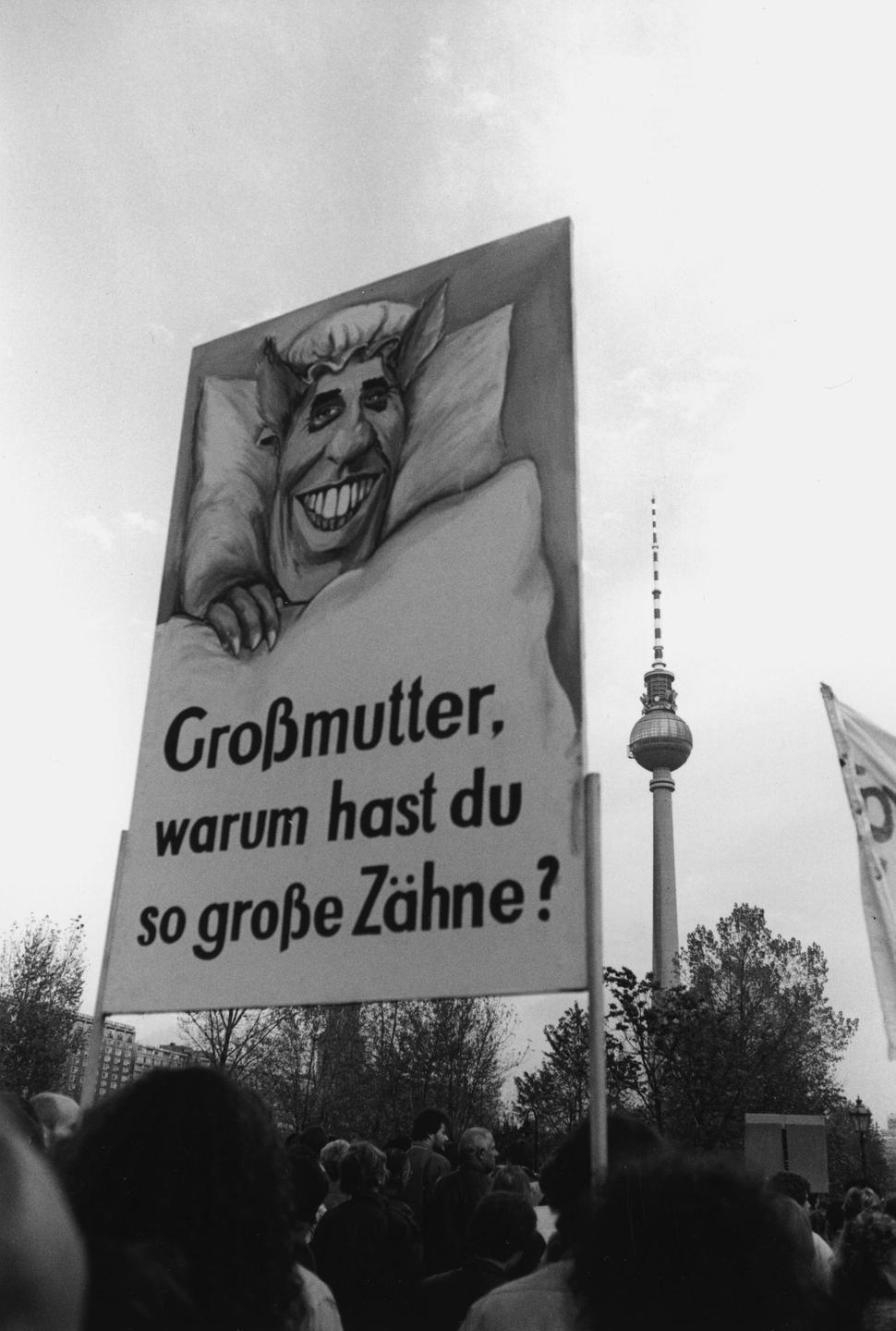 Demonstration in Ost-Berlin 4. November 1989. Eine Person hält ein Plakat in die Höhe, auf dem der DDR-Politiker Egon Krenz als Wolf aus dem Märchen Rotkäppchen dargestellt wird.