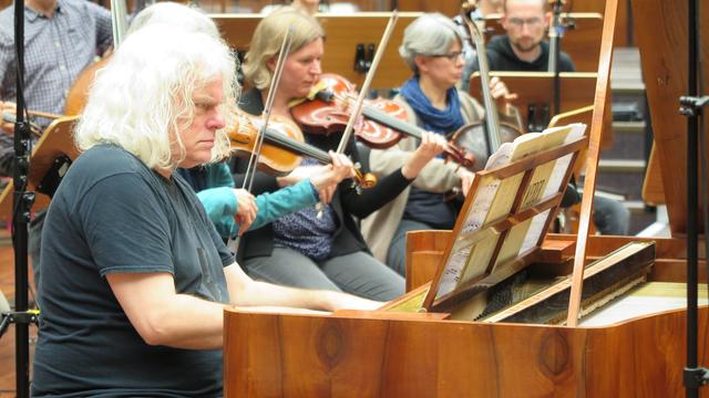 Der Pianist Jochen Hubmacher spielt mit ernster Miene. Im Hintergrund ein Orchester. 