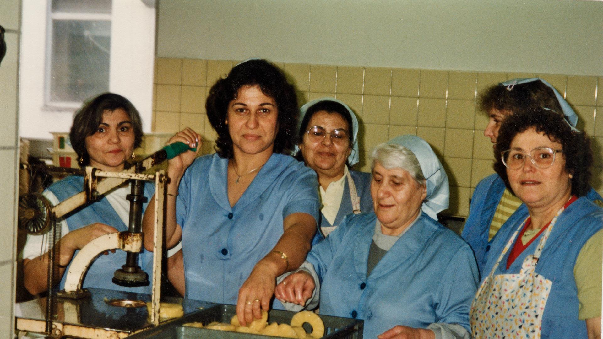 Frauen stehen in blauer Arbeitskleidung an einer Maschine. Arbeiterinnen bei Hachez. Frauen stehen in blauer Arbeitskleidung an einer Maschine. Arbeiterinnen bei Hachez.