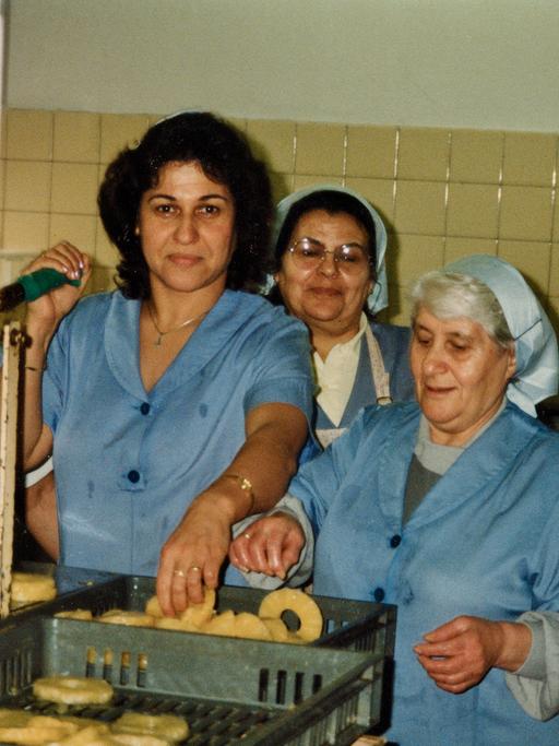 Frauen stehen in blauer Arbeitskleidung an einer Maschine. Arbeiterinnen bei Hachez.