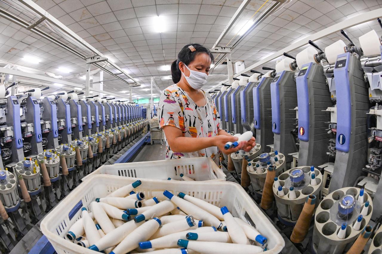 Ein Frau mit Spulen in einer großen Textilindustiehalle in China.