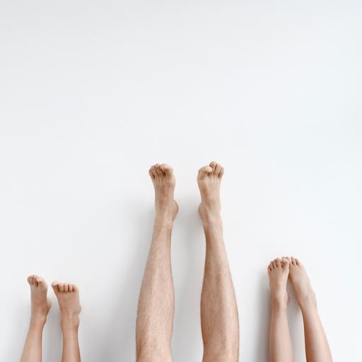 Drei Paar Beine mit den Füßen nach oben an eine Wand gestreckt. Das Paar in der Mitte gehört zu einem Erwachsenen und ist am längsten.