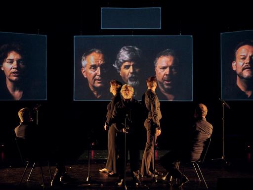 Vier schwarz gekleidete Männer stehen während einer Aufführung des Stückes "Die Einfachen" von Sergej Newski auf der Bühne.