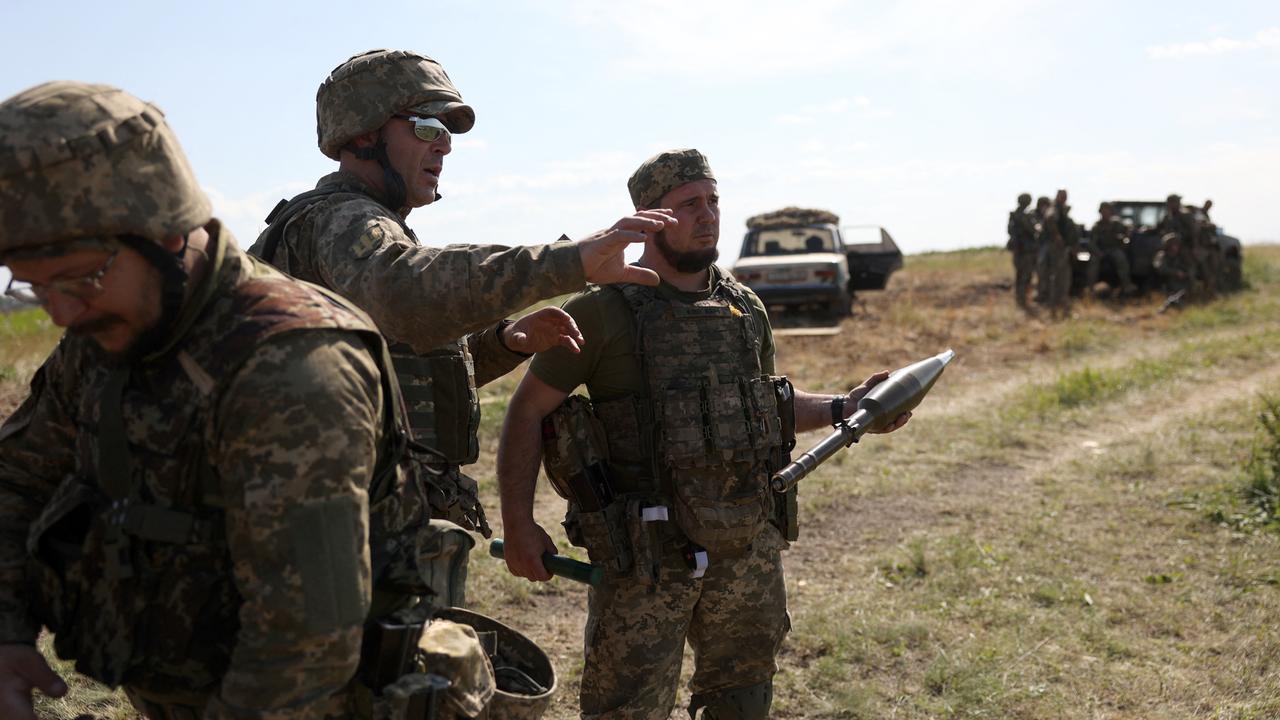 Ukrainische Soldaten stehen mit militärischem Gerät auf einem Feld.