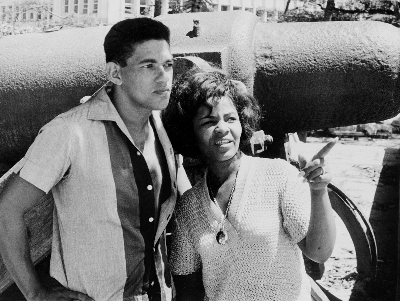 Fußballstar Garrincha und Musikstar Elza Soares stehen vor einem Flugzeug. Er hat auf dem Schwarz-Weiß-Bild seinen Arm um sie gelegt, sie zeigt mit ihrem linken Fußballstar Garrincha und Musikstar Elza Soares stehen vor einem Flugzeug. Er hat auf dem Schwarz-Weiß-Bild seinen Arm um sie gelegt, sie zeigt mit ihrem linken