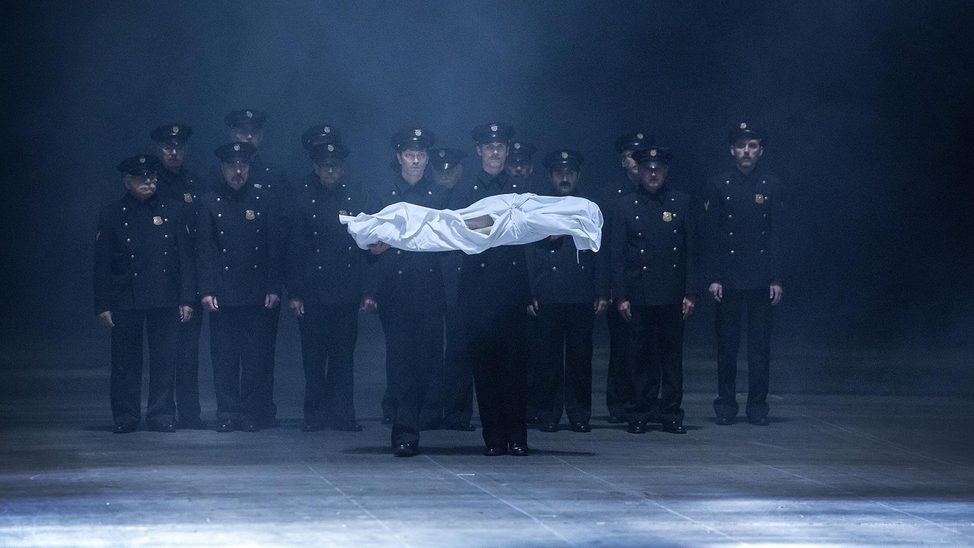 Eine Gruppe Männer in Polizeiuniformen trägt einen kleinen in weißes Tuch gehüllten Körper. Eine Gruppe Männer in Polizeiuniformen trägt einen kleinen in weißes Tuch gehüllten Körper.