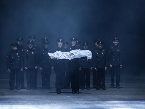 Eine Gruppe Männer in Polizeiuniformen trägt einen kleinen in weißes Tuch gehüllten Körper.