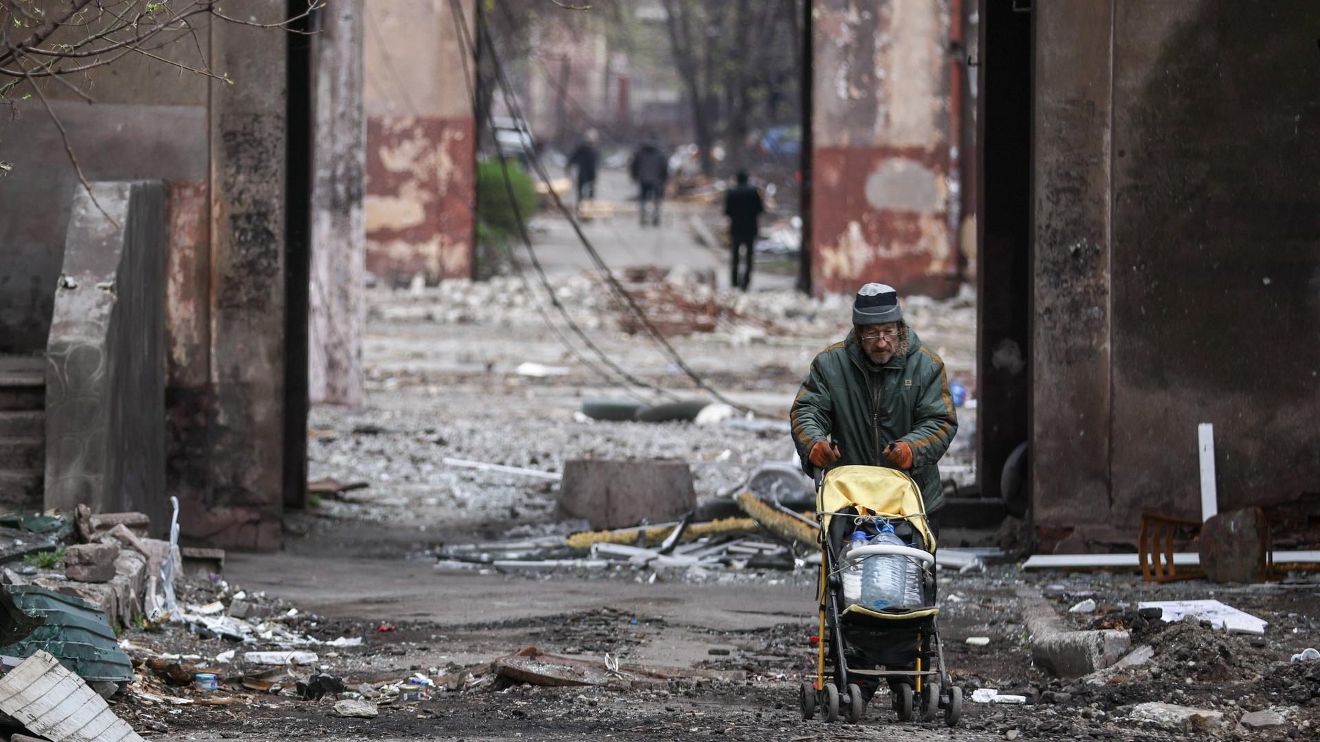 Im völlig zerstörten Mariupol schiebt ein Mann einen Kinderwagen und transportiert damit Plastikflaschen. Im völlig zerstörten Mariupol schiebt ein Mann einen Kinderwagen und transportiert damit Plastikflaschen.