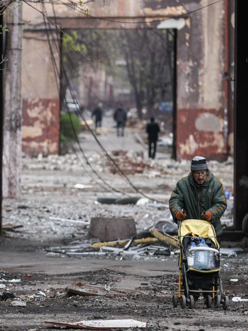Im völlig zerstörten Mariupol schiebt ein Mann einen Kinderwagen und transportiert damit Plastikflaschen.