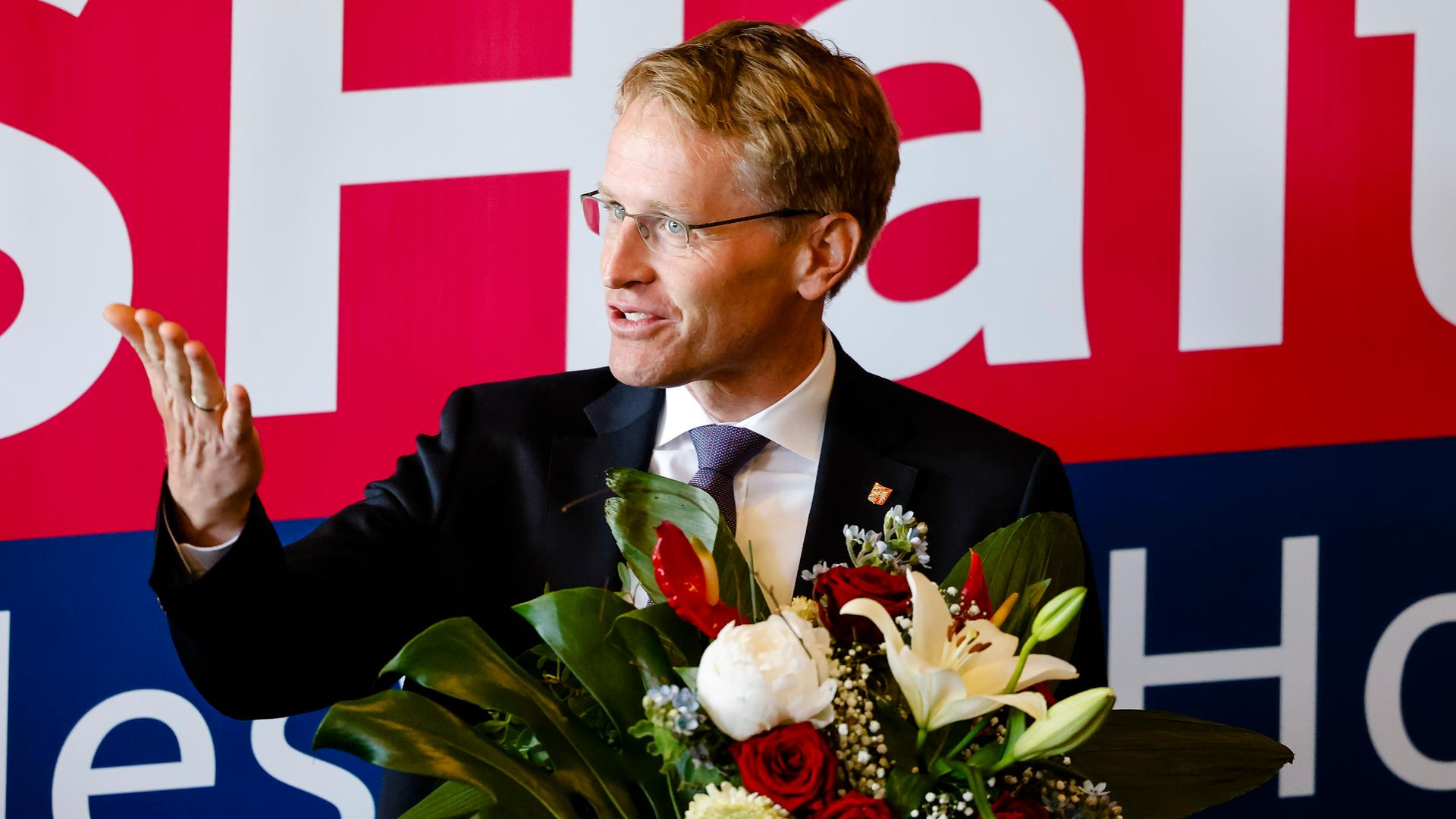 Minister-Präsident Daniel Günther hält einen Blumenstrauß und lächelt. Minister-Präsident Daniel Günther hält einen Blumenstrauß und lächelt.