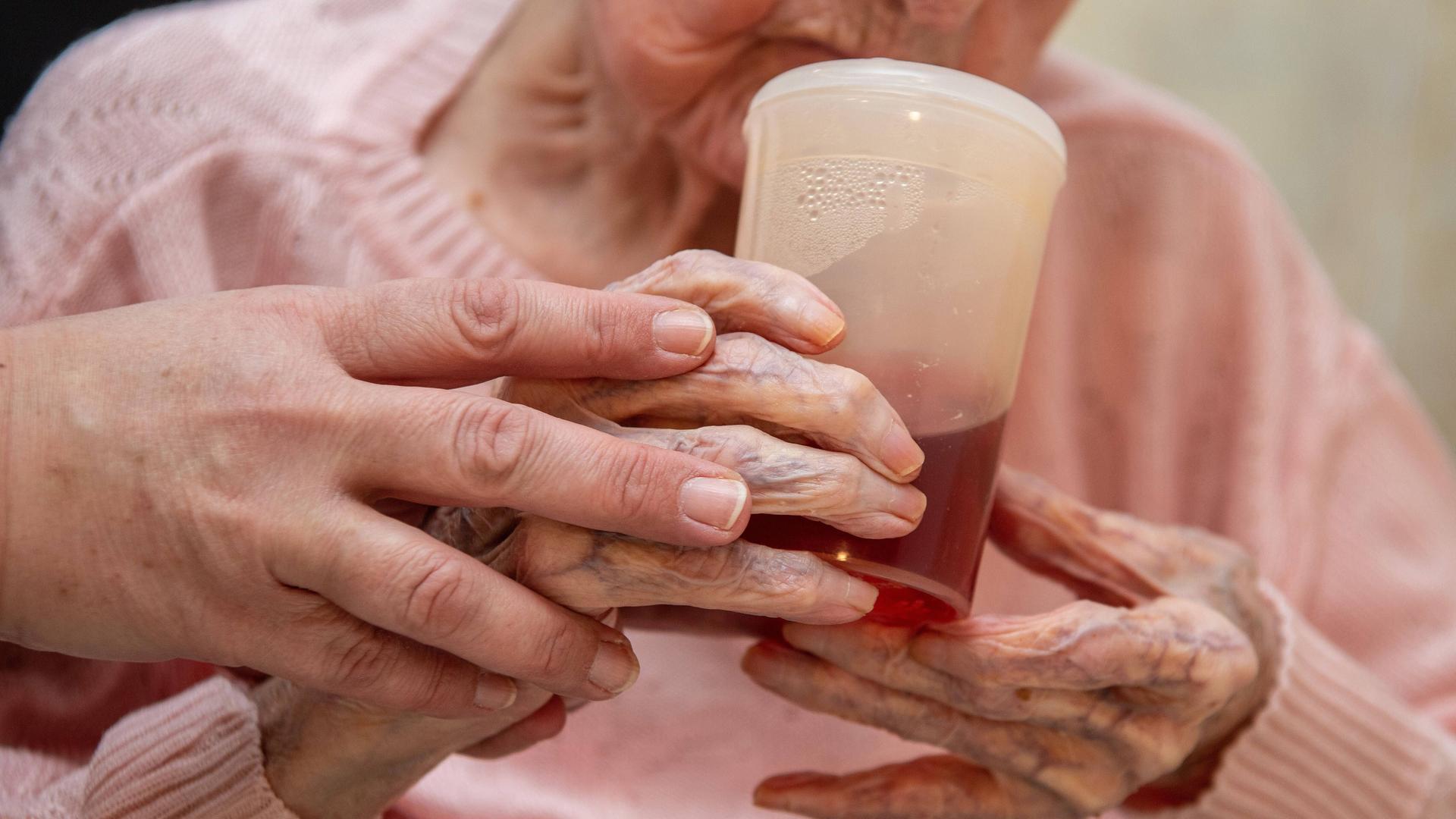 Eine Altenpflegerin hilft einer Seniorin beim halten eines Trinkbechers Eine Altenpflegerin hilft einer Seniorin beim halten eines Trinkbechers