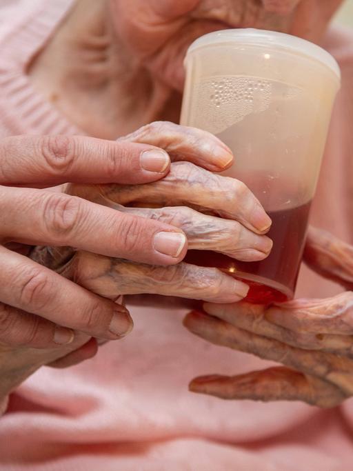 Eine Altenpflegerin hilft einer Seniorin beim halten eines Trinkbechers