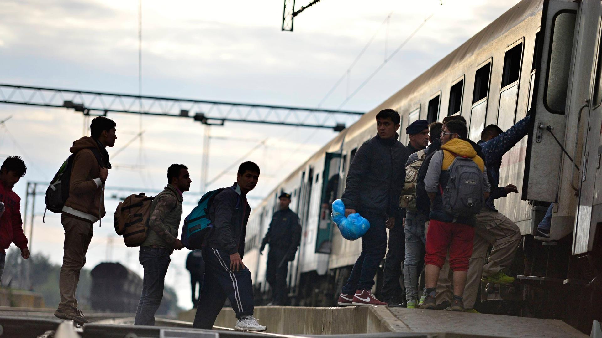 Flüchtlinge stehen auf Bahngleisen und besteigen einen Zug. Dabei werden sie von der Polizei begleitet. Flüchtlinge stehen auf Bahngleisen und besteigen einen Zug. Dabei werden sie von der Polizei begleitet.