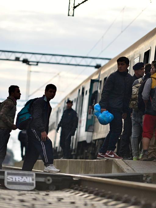 Flüchtlinge stehen auf Bahngleisen und besteigen einen Zug. Dabei werden sie von der Polizei begleitet.