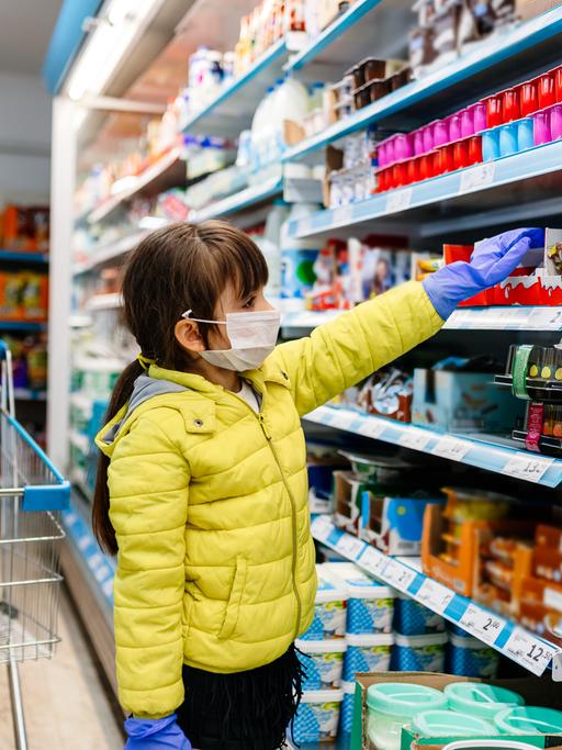 Mutter und Tochter beim Einkauf mit Maske und Handschuhen, der Einkaufswagen ist fast leer.