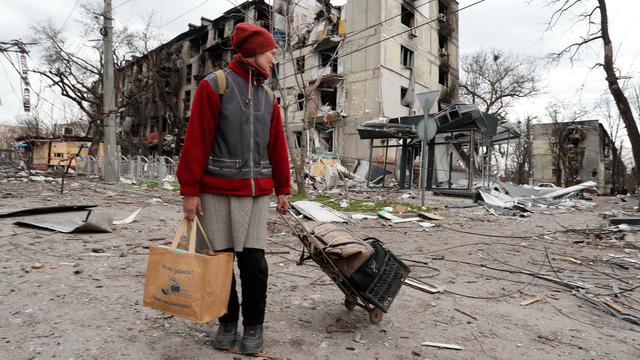 Ukraine, Mariupol: Eine Anwohnerin geht mit Gepäck an einem beschädigten Wohnhaus vorbei.
