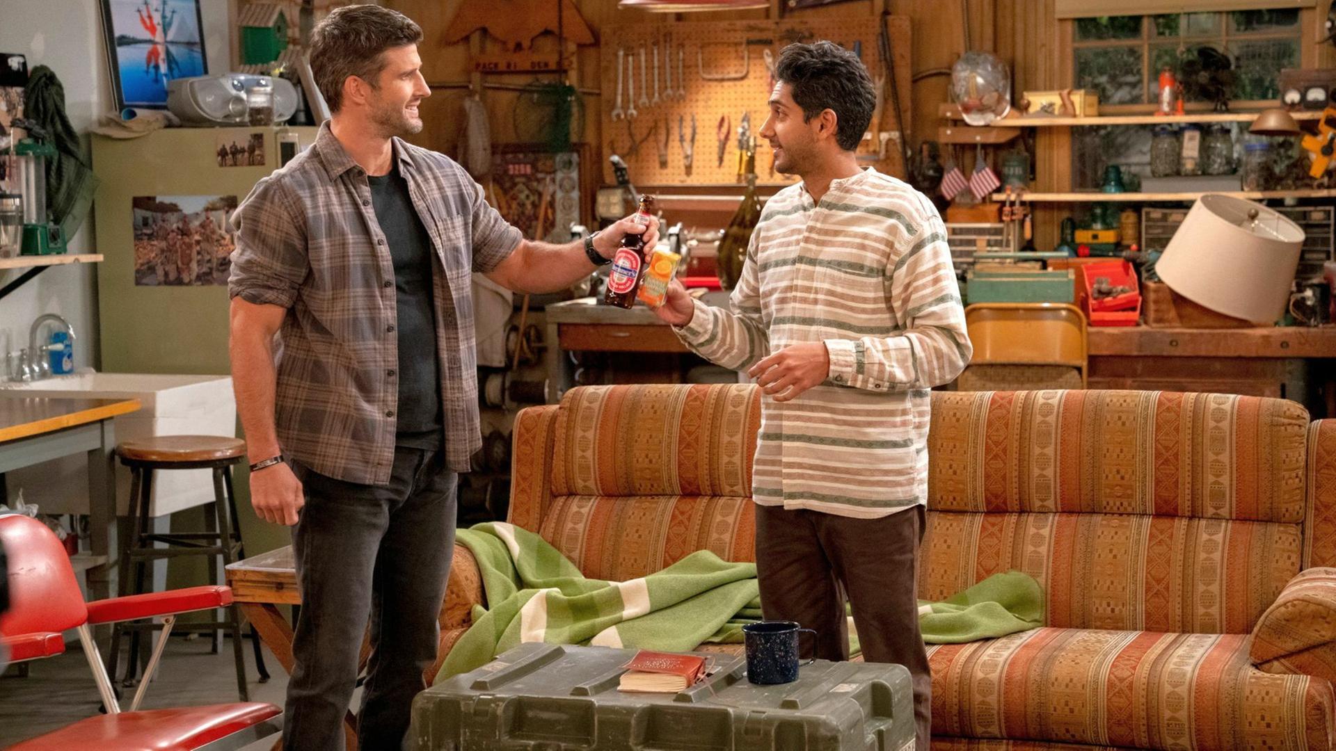 Im Still aus "United States of Al" stehen die beiden Protagonisten in einem Wohnzimmer vor einem Sofa und stoßen mit Bier und Limonade an.