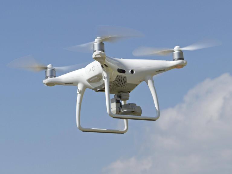 Zivile Drohnenpilotinnen in Konfliktsituation. Zu sehen: Eine fliegende Drohne mit Kamera. 