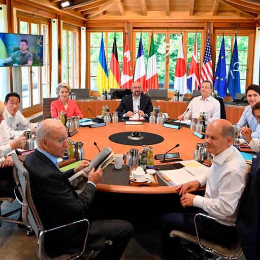 Die Runde des G7-Gipfels in Elmau. Und einen Konferenztisch sitzen die Regierungschefs der USA (Joe Biden), Deutschlands (Olaf Scholz), Frankreichs (Emmanuel Macron), Italiens (Mario Draghi), Großbritanniens (Boris Johnson), Kanadas (Justin Trudeau) und Japans (Fumio Kishida) mit der EU-Kommissionspräsidenten Ursula von der Leyen und EU-Ratspräsident Charles Michel. Im HIntergrund ist auf einem Vi
