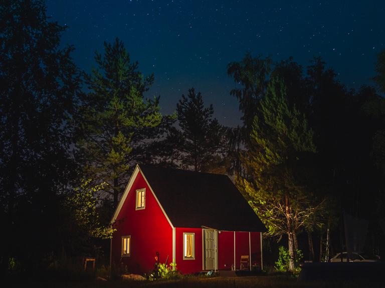 Ein kleines rotes Haus bei Nacht in einem Wald.