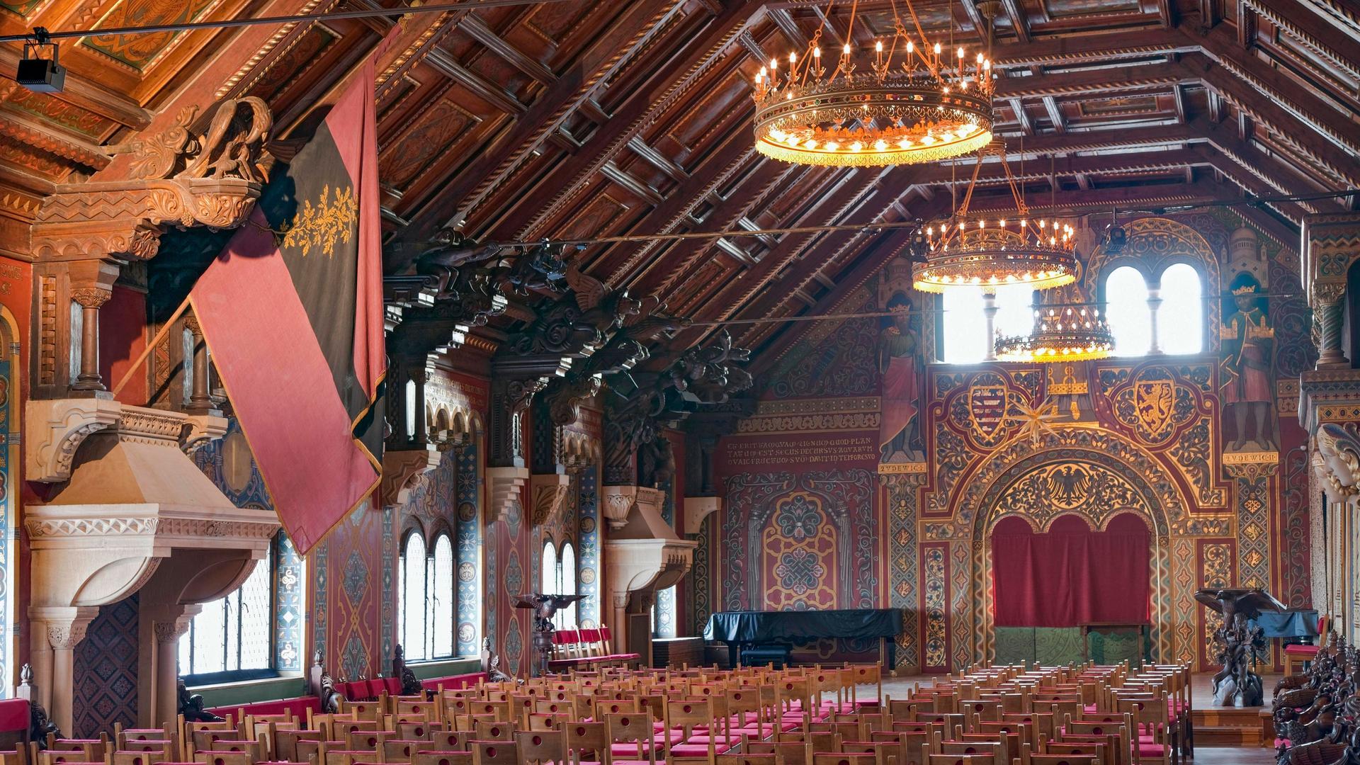 Blick in den mit Holz ausgetäfelten und mit vielen Fenstern bestückte lange Saal, in dem viele Zuschauerstühle stehen. Blick in den mit Holz ausgetäfelten und mit vielen Fenstern bestückte lange Saal, in dem viele Zuschauerstühle stehen.