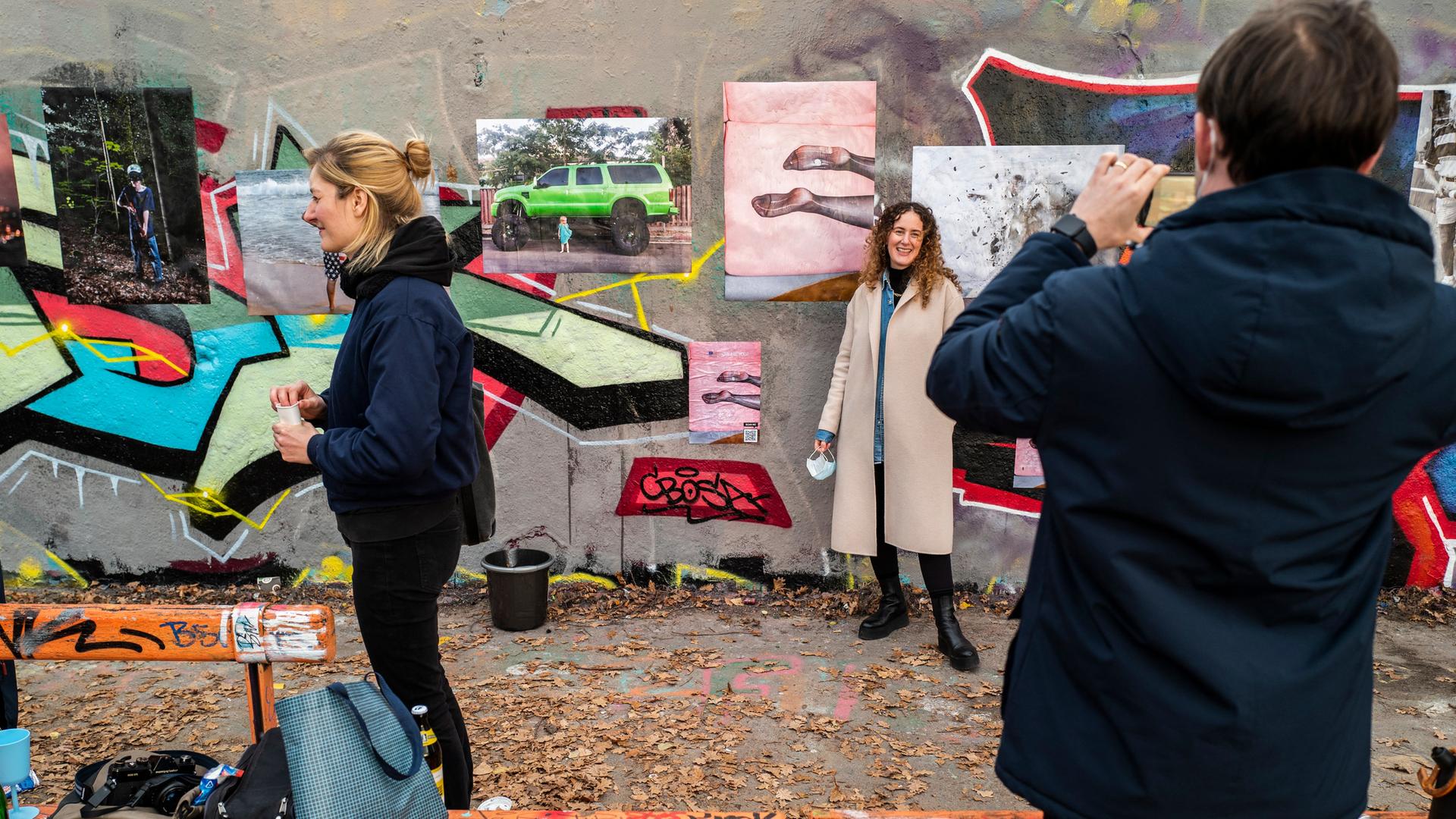 Drei Personen sind vor einer Austellung des Fotografinnen-Kollektivs "herspective" auf einem Teil der früheren Berliner Mauer unter freiem Himmel im Berliner Mauerpark zu sehen. Eine Person fotografiert eine andere. Drei Personen sind vor einer Austellung des Fotografinnen-Kollektivs "herspective" auf einem Teil der früheren Berliner Mauer unter freiem Himmel im Berliner Mauerpark zu sehen. Eine Person fotografiert eine andere.