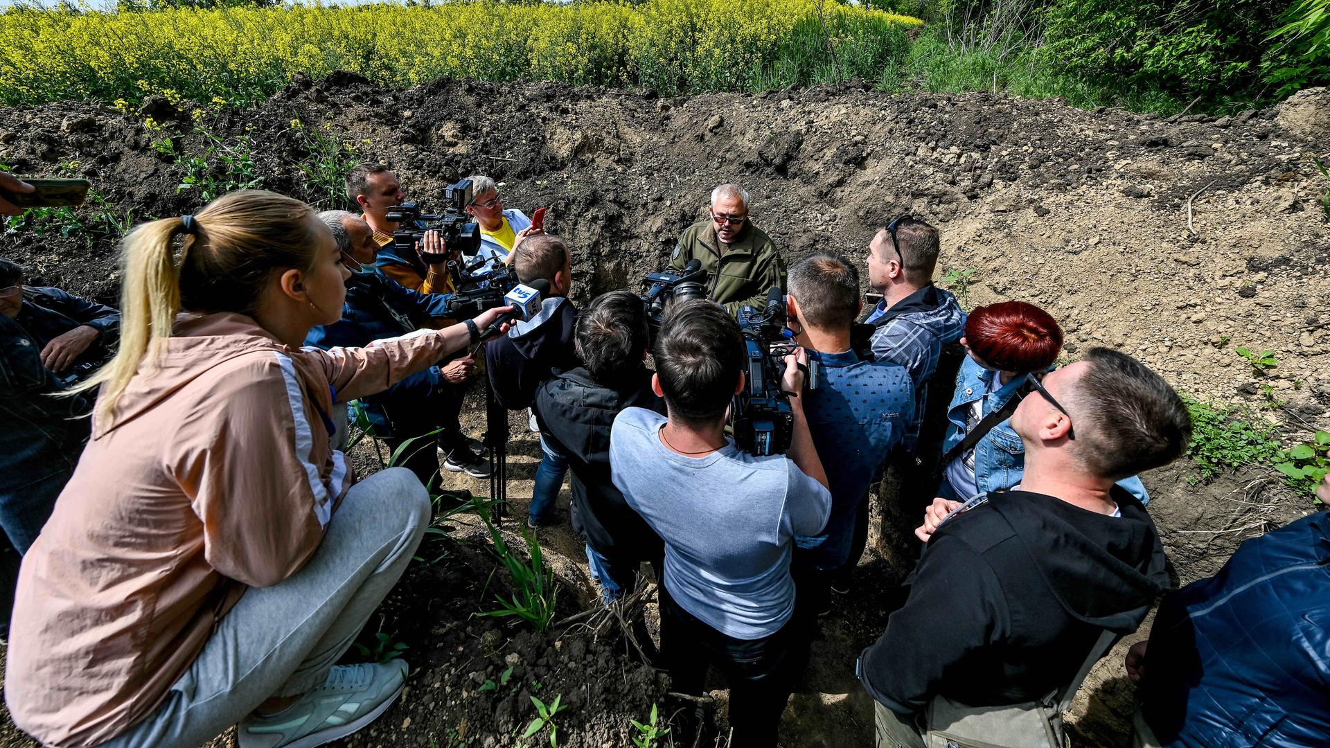 Medienvertreter sitzen im Kreis um einen ukrainischen Militär im Feld. Medienvertreter sitzen im Kreis um einen ukrainischen Militär im Feld.