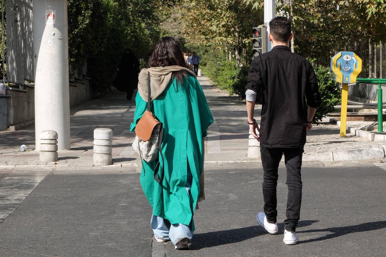 Ein junges iranisches Paar läuft auf einer Strasse in Teheran, von hinten zu sehen. Ihr Kopftuch liegt locker auf ihren Schultern als Ausdruck von Protest gegen die Moralgesetze des Landes. Teheran, 28. September 2022. Ein junges iranisches Paar läuft auf einer Strasse in Teheran, von hinten zu sehen. Ihr Kopftuch liegt locker auf ihren Schultern als Ausdruck von Protest gegen die Moralgesetze des Landes. Teheran, 28. September 2022.