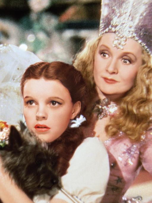 In dem Szenenbild von "Der Zauberer von Oz" schaut Judy Garland in der Rolle der "Dorothy" gebannt nach vorn, hinter ihr steht Billie Burke als 'Glinda'.